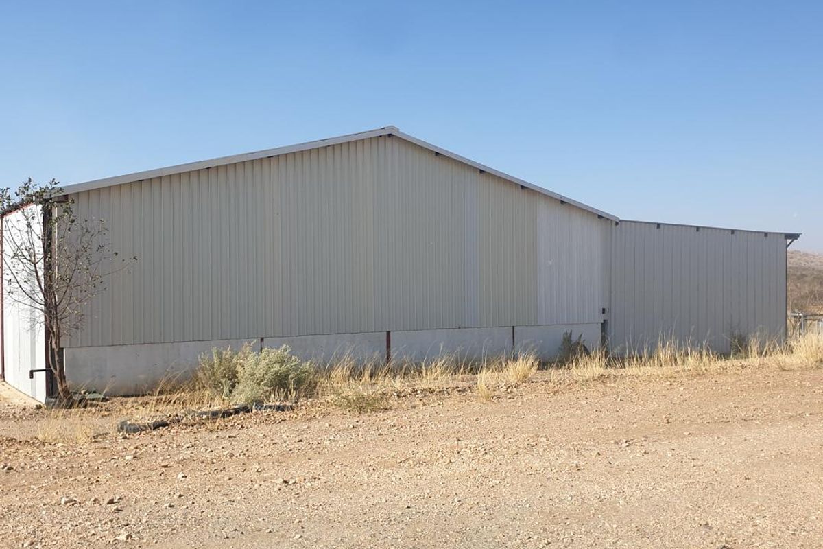 Side view of a large industrial warehouse structure featuring corrugated metal cladding and a concrete base, situated on a gravel lot.