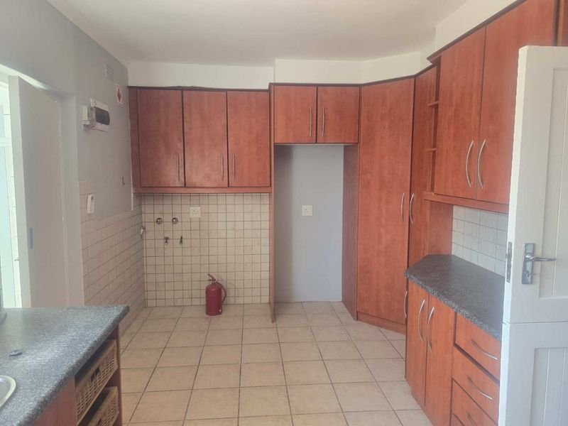 A functional kitchen featuring wood-look cabinetry, tiled flooring, a tiled backsplash, and dedicated space for appliances.