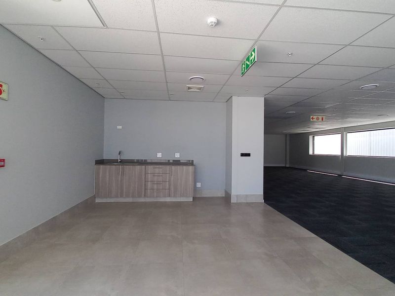 Spacious open-plan industrial office area featuring a built-in kitchenette, suspended ceilings, and a combination of tiled and carpeted flooring.