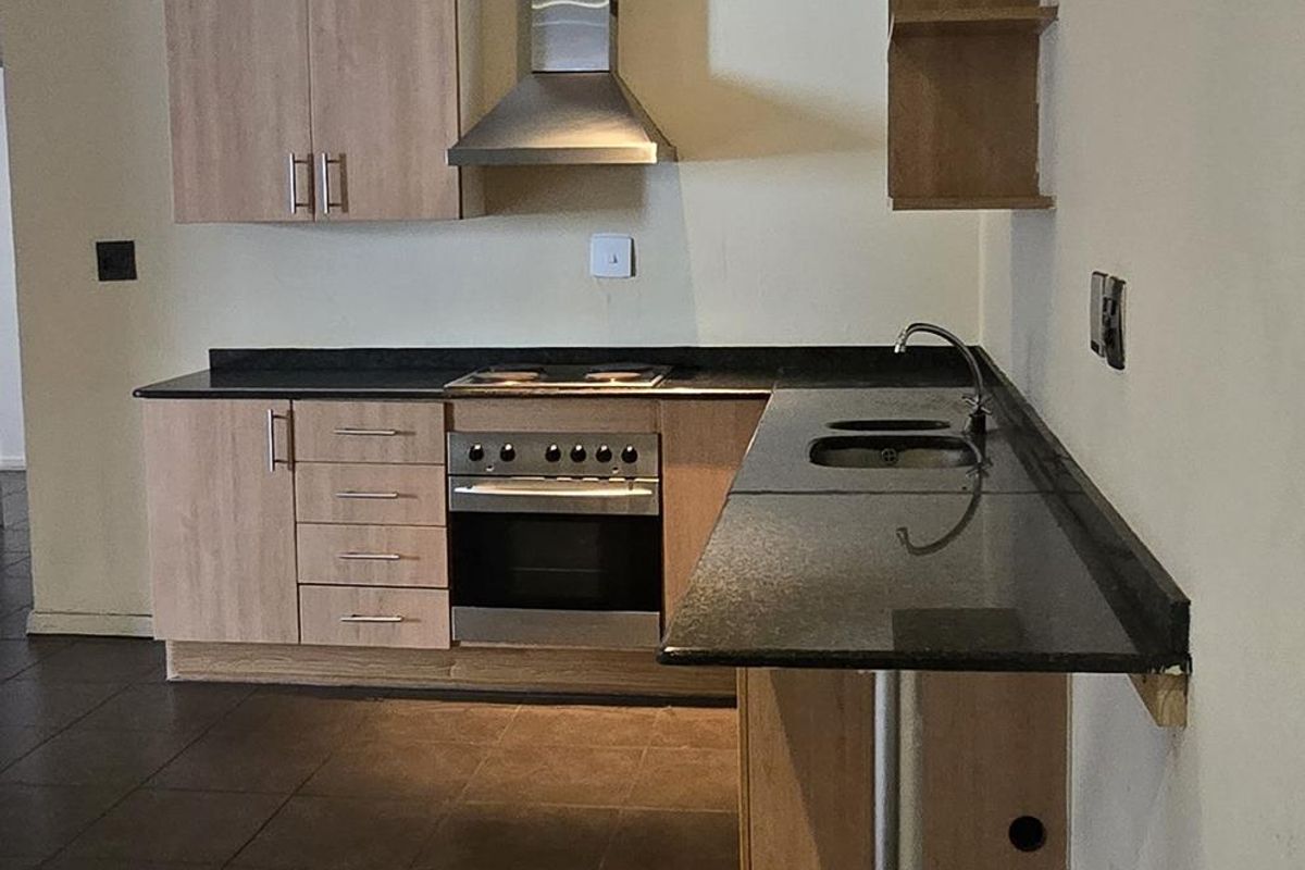 A functional kitchen featuring light wood cabinetry, granite countertops, a built-in oven, and a stainless steel extractor fan with tiled flooring.