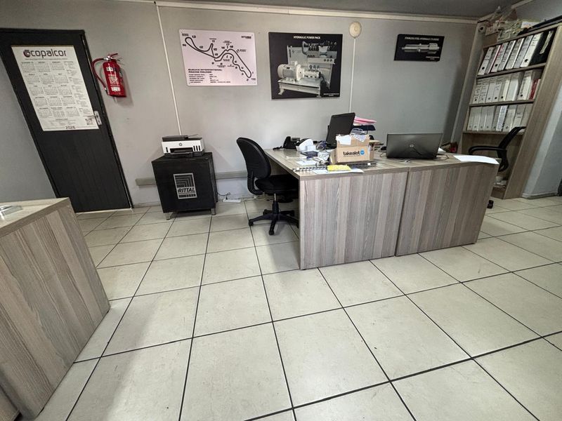 A functional industrial office space featuring tiled flooring, built-in shelving, and a wall-mounted fire extinguisher.