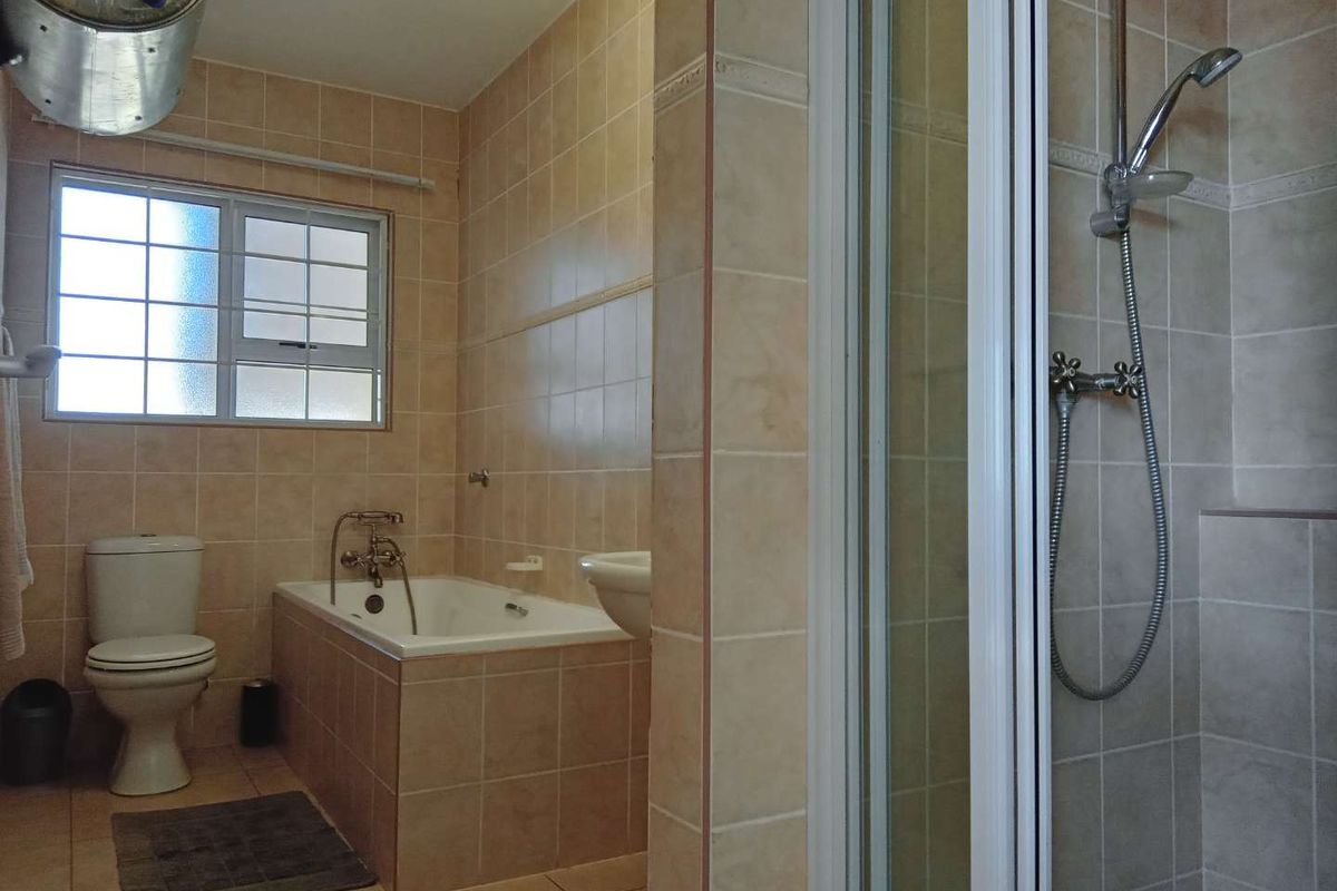 A functional bathroom featuring a tiled bathtub, separate shower enclosure, and toilet, finished with neutral wall and floor tiles.