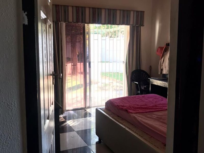 Bedroom featuring exposed timber ceiling beams, checkered tiled flooring, and a sliding glass door with security gate providing access to the exterior.