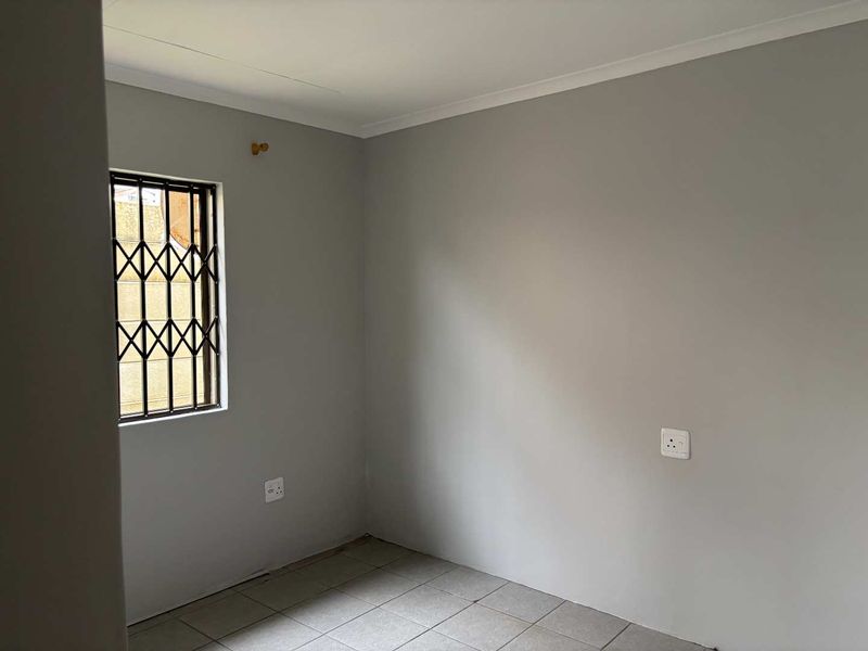 A clean, empty bedroom featuring neutral grey walls, tiled flooring, and a window fitted with a security gate.