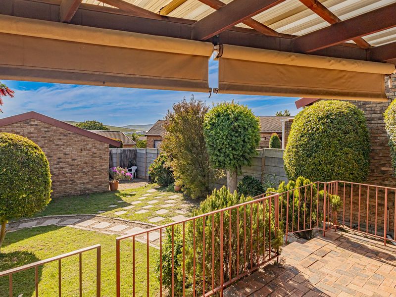 A covered patio area featuring a timber pergola, retractable awning, and metal balustrade, overlooking a private garden with brick paving and established landscaping.