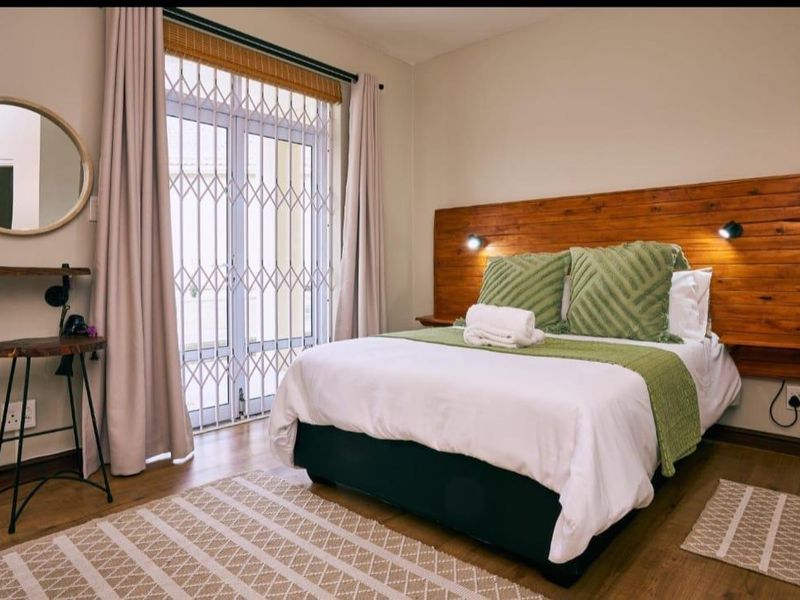 A well-maintained bedroom featuring laminate flooring, a custom wooden headboard with integrated lighting, and a sliding door with a security gate.