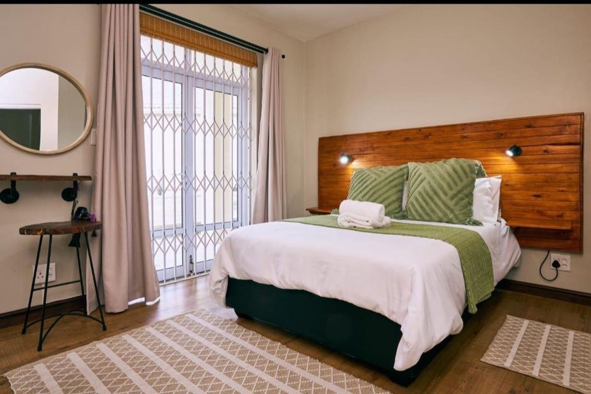 A well-maintained bedroom featuring laminate flooring, a custom wooden headboard with integrated lighting, and a sliding door with a security gate.