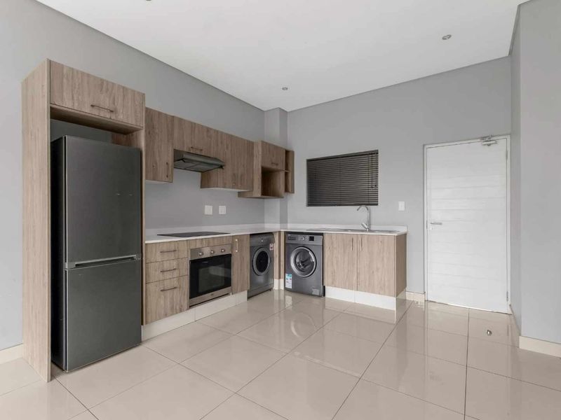 Modern kitchen featuring light wood-tone cabinetry, integrated oven and hob, stainless steel sink, and sleek tiled flooring in an open-plan layout.