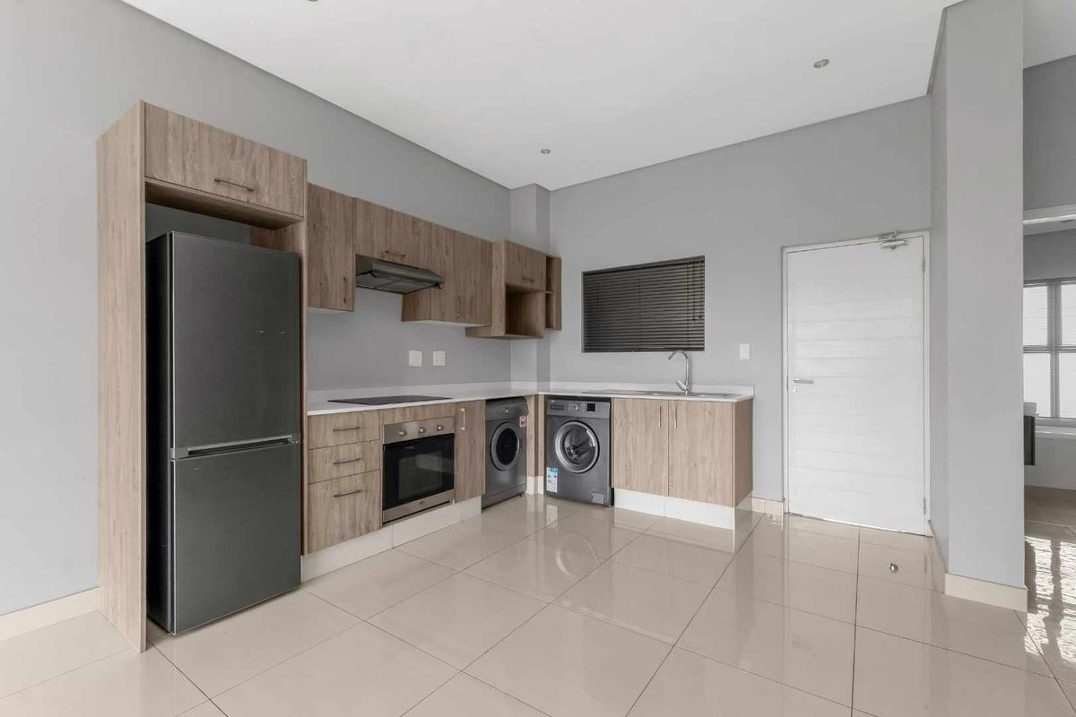 Modern kitchen featuring light wood-tone cabinetry, integrated oven and hob, stainless steel sink, and sleek tiled flooring in an open-plan layout.