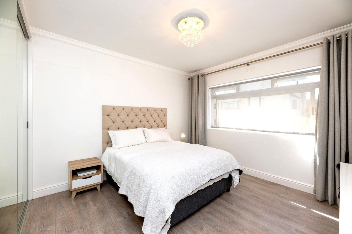 A well-maintained bedroom featuring laminate flooring, a built-in sliding door wardrobe, and a large window with curtain rails.