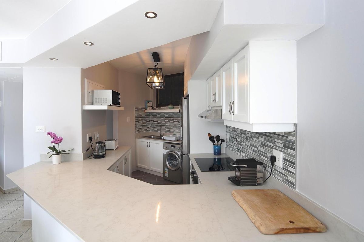 Modern kitchen featuring white cabinetry, stone countertops, mosaic tile backsplash, integrated hob, and built-in extractor fan with recessed ceiling lighting.