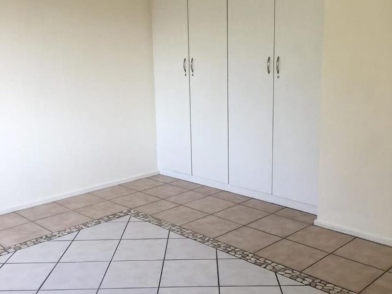 An empty bedroom featuring built-in cupboards and a tiled floor with a decorative pebble border detail.