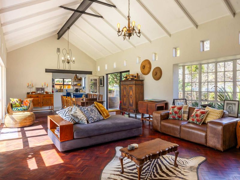 Spacious open-plan living area featuring a high vaulted ceiling with exposed beams, rich herringbone parquet flooring, and abundant natural light from large windows.