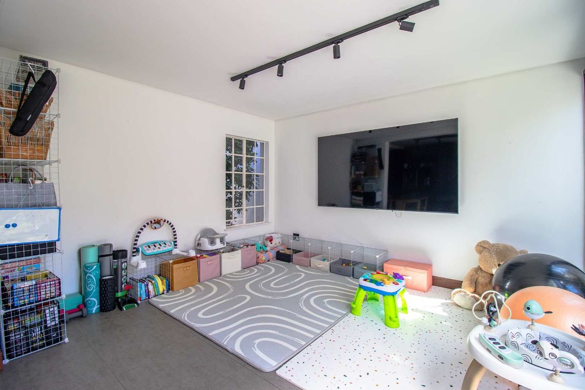 A versatile living space featuring modern track lighting, large wall-mounted television, and neutral tiled flooring, currently utilized as a play area.