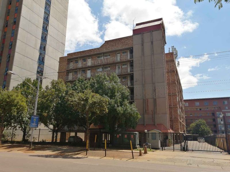 Street view of a multi-story apartment building featuring a brick facade, private balconies, and a secure gated entrance.