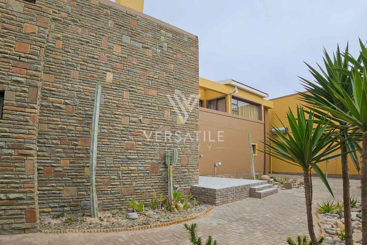 Rear exterior view of the property featuring stone cladding, paved courtyard area, and a raised patio section.