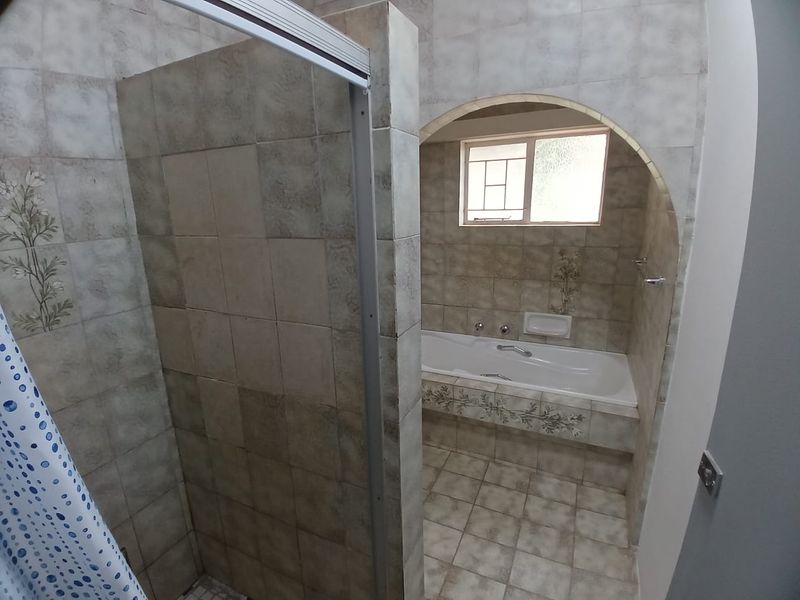 A dated bathroom featuring a built-in bathtub, a separate shower enclosure, and an arched entryway, finished with neutral patterned wall tiles.