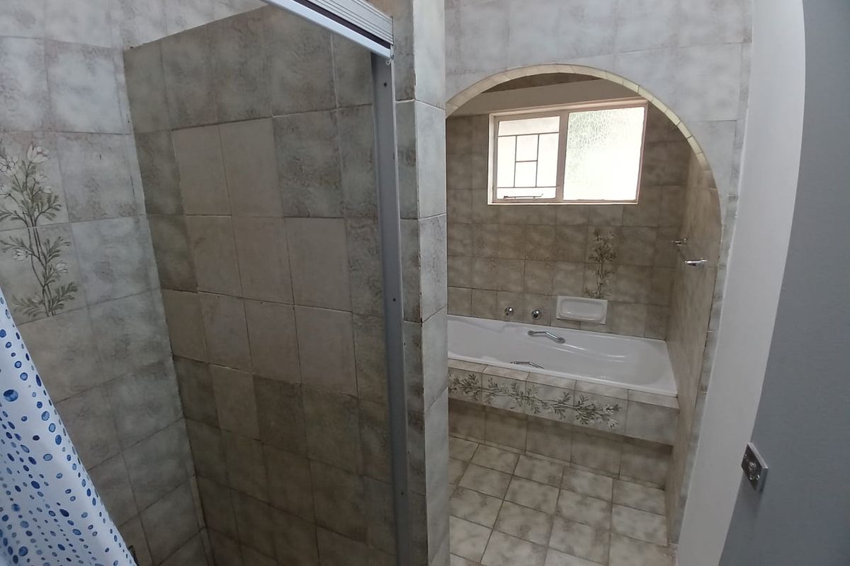 A dated bathroom featuring a built-in bathtub, a separate shower enclosure, and an arched entryway, finished with neutral patterned wall tiles.