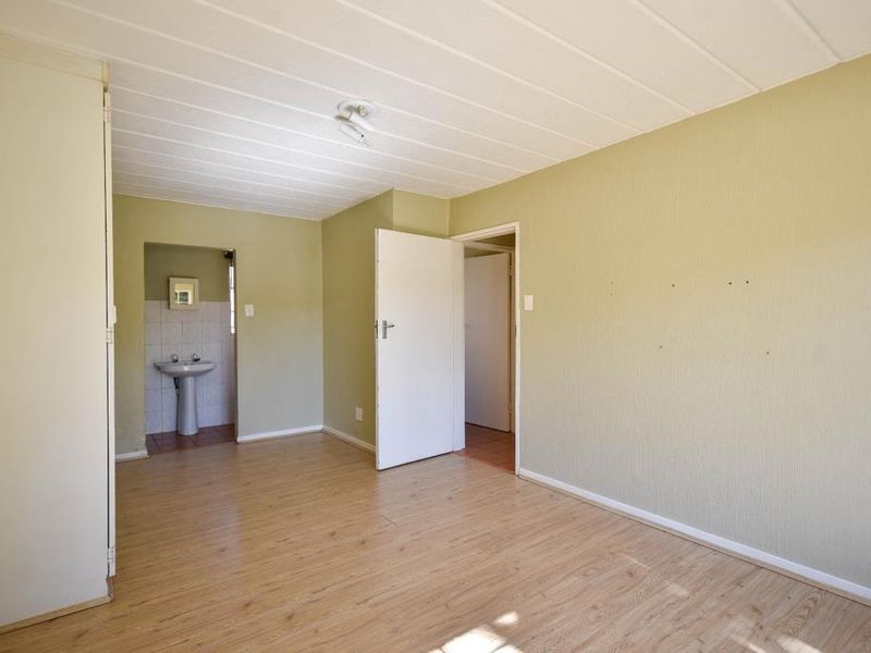 An empty bedroom featuring laminate flooring, a small en-suite area with a pedestal basin, and built-in storage.