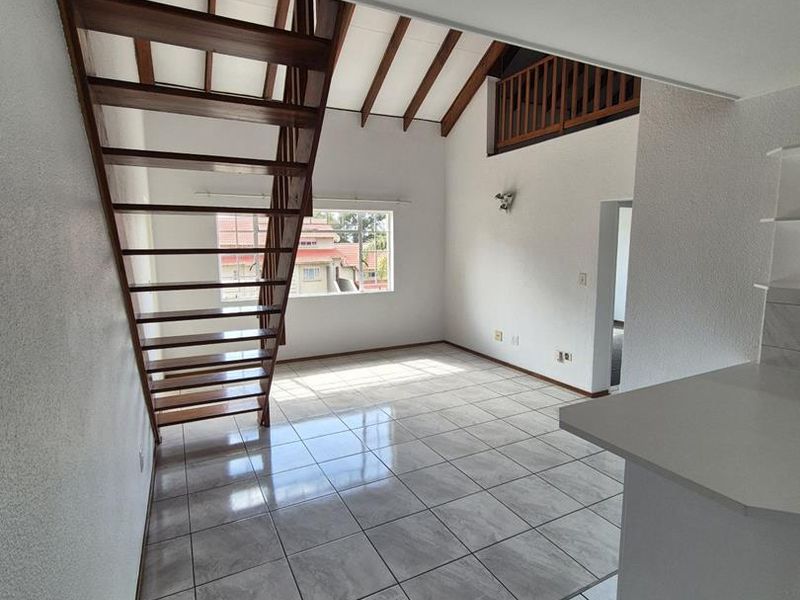 Spacious open-plan living area featuring a striking timber staircase, vaulted ceilings with exposed beams, and a mezzanine level overlooking the tiled main floor.