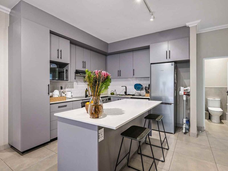 Modern kitchen featuring grey cabinetry, a central island with stone countertop, subway tile backsplash, and integrated appliances, leading to an adjacent bathroom.