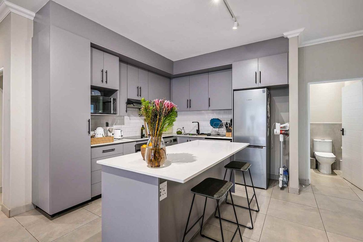 Modern kitchen featuring grey cabinetry, a central island with stone countertop, subway tile backsplash, and integrated appliances, leading to an adjacent bathroom.