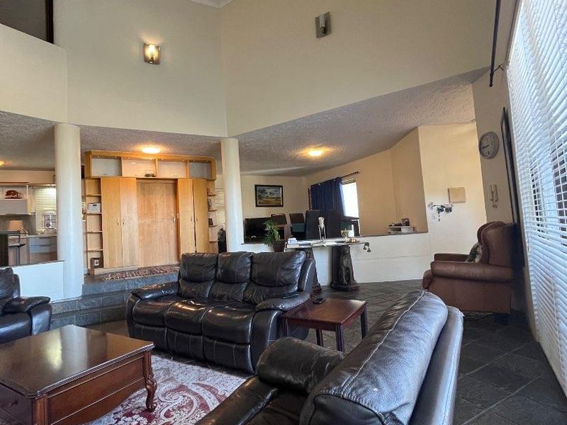 Spacious open-plan living area featuring high vaulted ceilings, slate tile flooring, and integrated cabinetry, offering a versatile layout with abundant natural light.