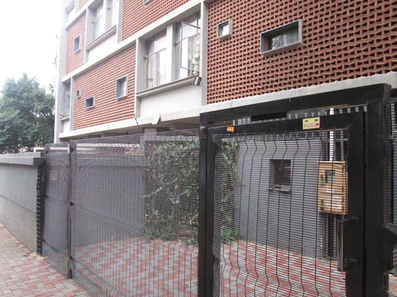 Exterior view of the apartment building facade featuring brickwork, security fencing, and a paved entrance area.