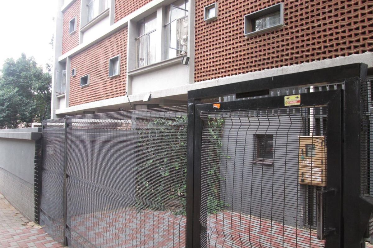 Exterior view of the apartment building facade featuring brickwork, security fencing, and a paved entrance area.