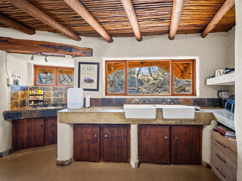 Rustic kitchen featuring exposed timber beam ceilings, concrete countertops with double farmhouse sinks, slate tile backsplash, and built-in wooden cabinetry.