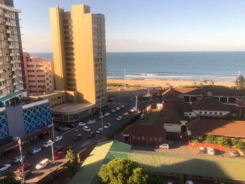 Elevated urban and coastal view overlooking the beach, surrounding apartment buildings, and street infrastructure.