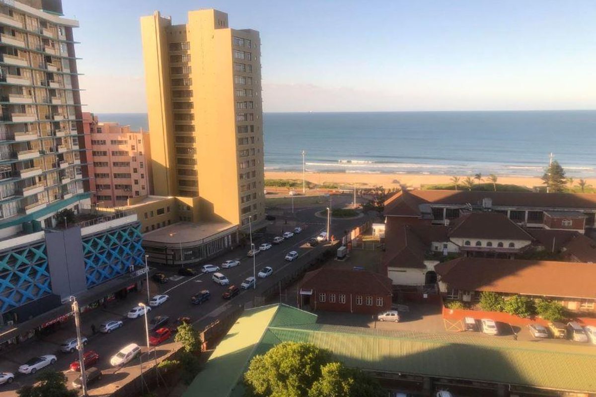 Elevated urban and coastal view overlooking the beach, surrounding apartment buildings, and street infrastructure.