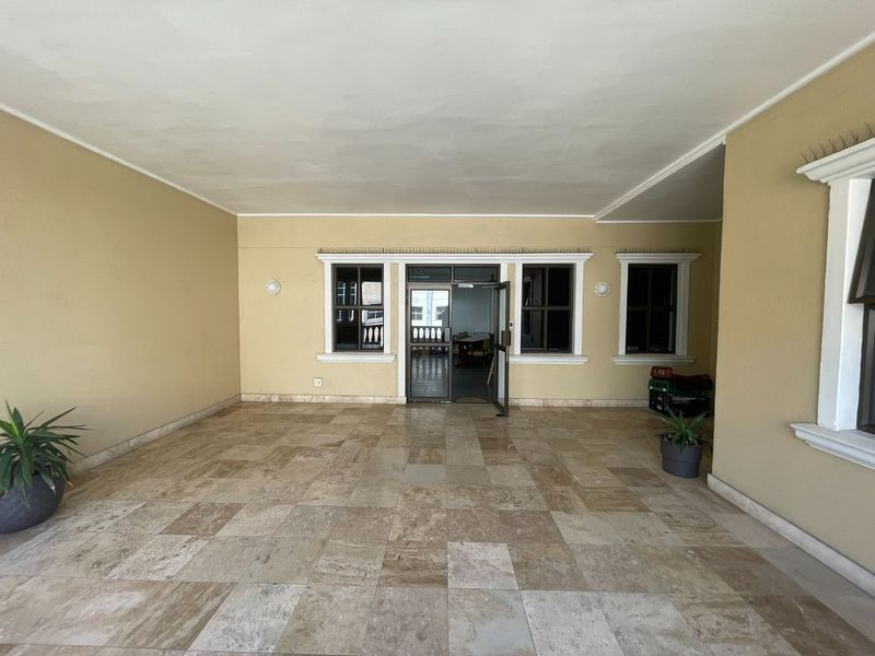 A spacious covered patio area featuring natural stone tiled flooring, neutral wall finishes, and direct access to the office interior through an aluminium door.