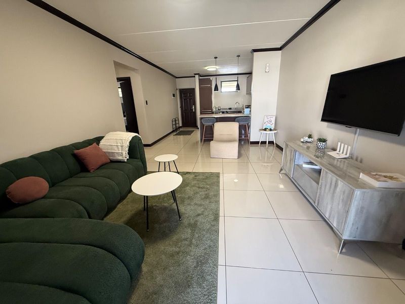 An open-plan living area featuring polished porcelain floor tiles, a breakfast bar, and a functional kitchen layout with modern pendant lighting.
