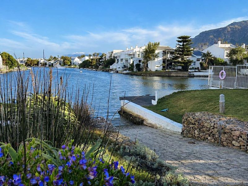 Scenic waterfront view overlooking the estate canal with landscaped gardens, stone retaining walls, and paved pathways leading to the water's edge.