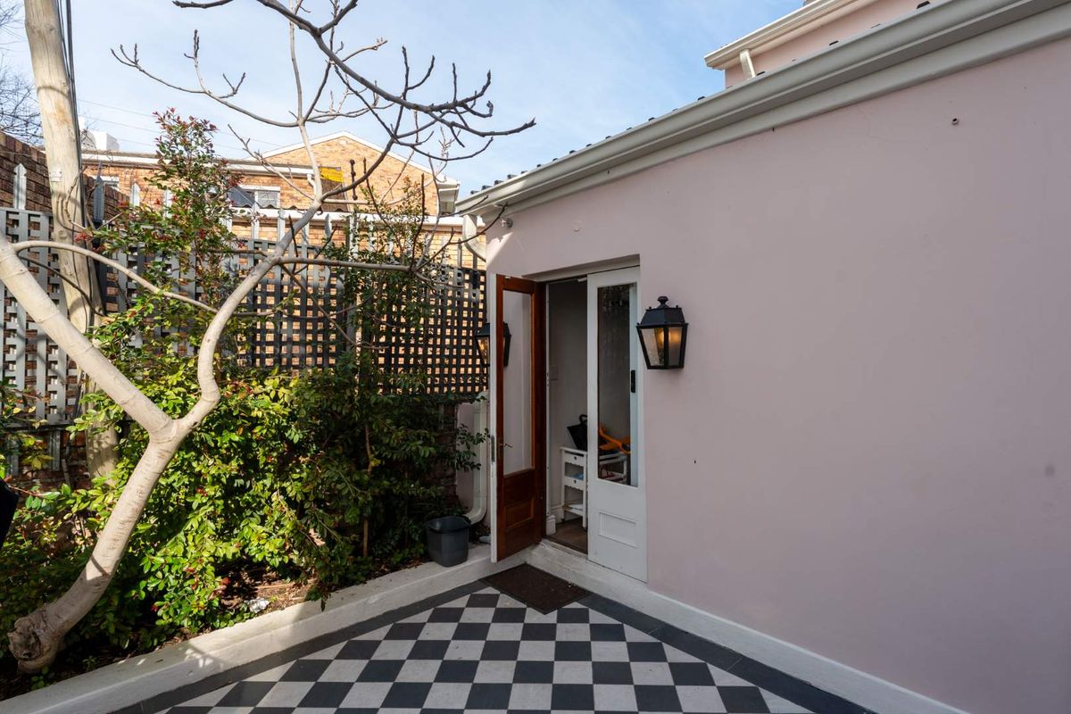 A charming rear courtyard featuring a classic black and white checkered tile patio, exterior wall lighting, and a timber-framed glass entrance door.