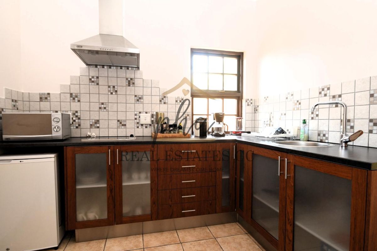 Functional kitchen featuring wood-finish cabinetry, dark countertops, tiled backsplash, stainless steel extractor fan, and a single basin sink.