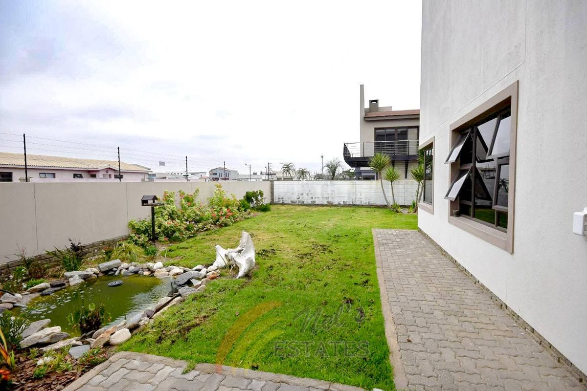 A rear garden area featuring a small pond, paved walkway, and perimeter boundary wall.