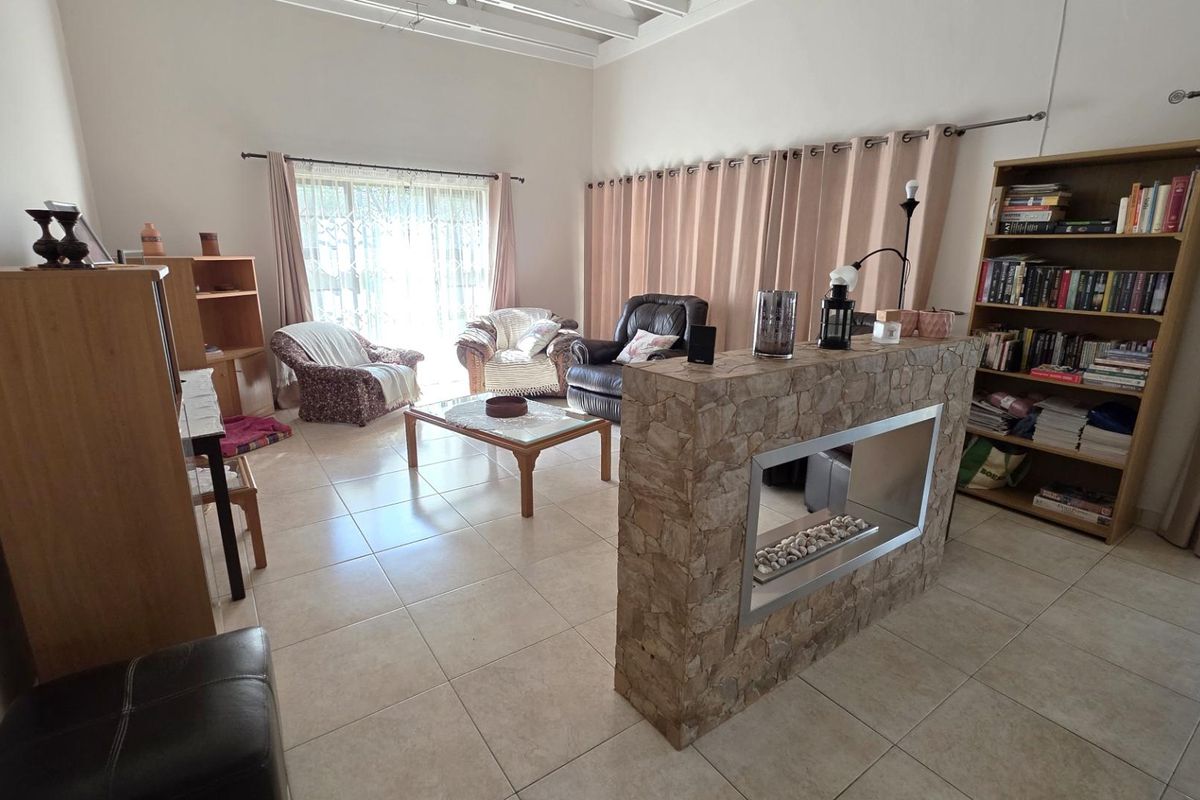 Spacious living area featuring a central stone-clad fireplace partition, tiled flooring, and large windows with curtain treatments.