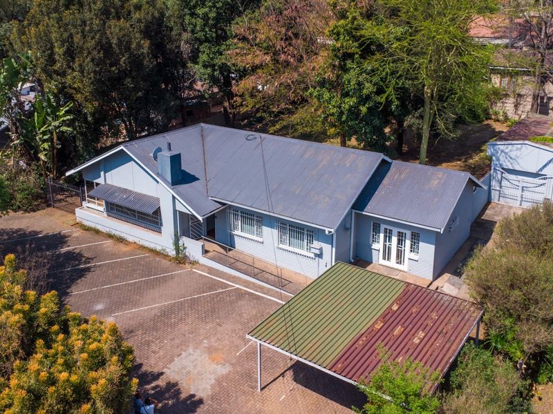 Aerial view of the property featuring a main house with a corrugated metal roof, paved driveway, and a detached garage with a carport.