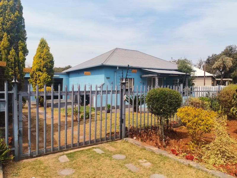 Front view of a single-story house featuring a metal roof, security fencing, and a gated driveway entrance.