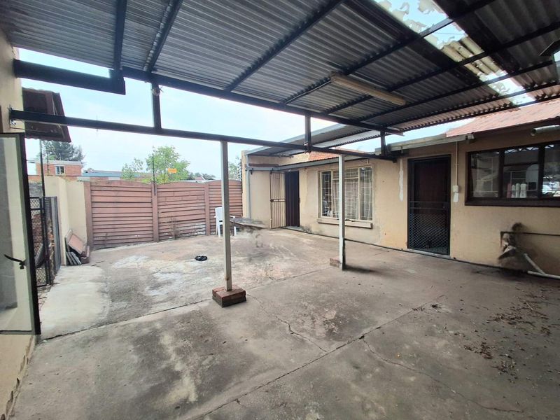 A covered outdoor patio area featuring a corrugated metal roof, concrete flooring, and direct access to the main dwelling through security doors.