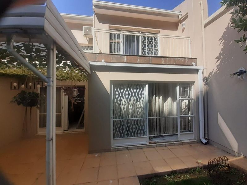 Rear view of the townhouse featuring a tiled patio area, sliding door access, and an upper-level balcony with security gates.