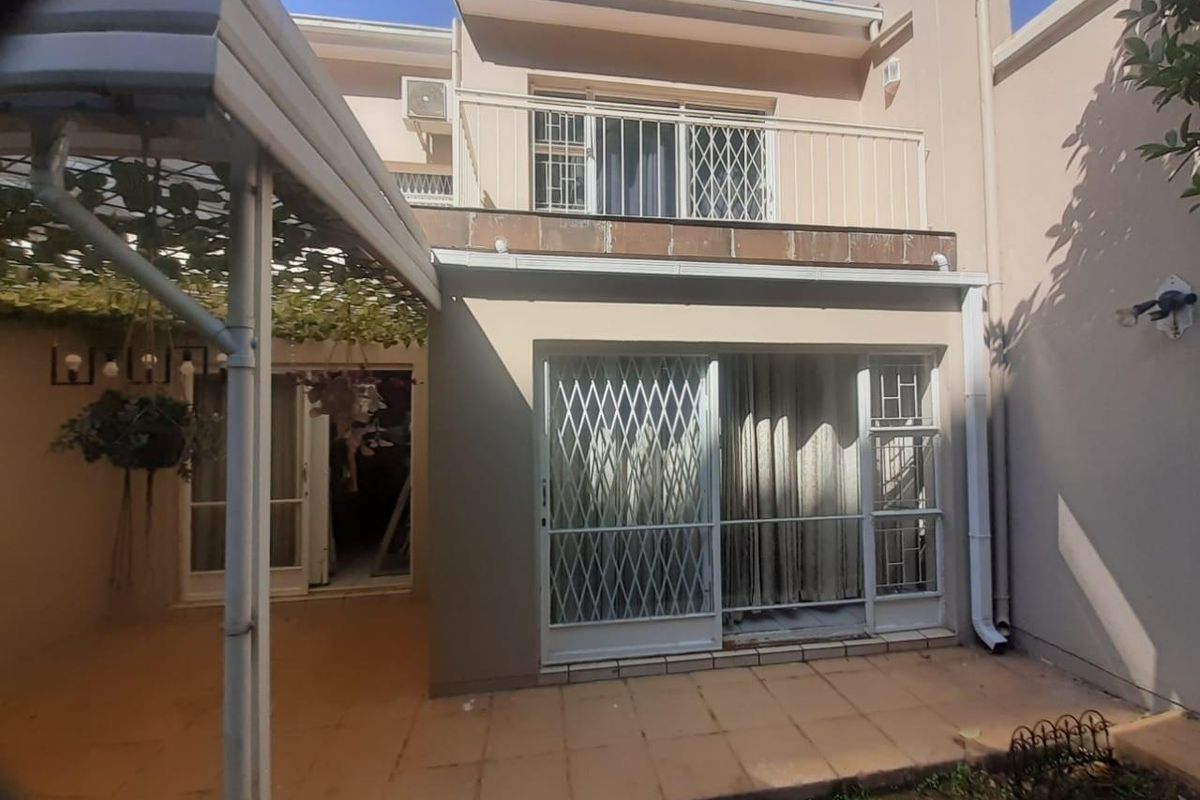 Rear view of the townhouse featuring a tiled patio area, sliding door access, and an upper-level balcony with security gates.