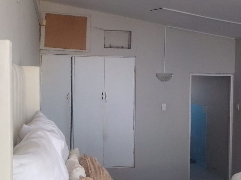 A bedroom featuring built-in cupboards and wall-mounted lighting, currently showing signs of unfinished maintenance and exposed electrical wiring.