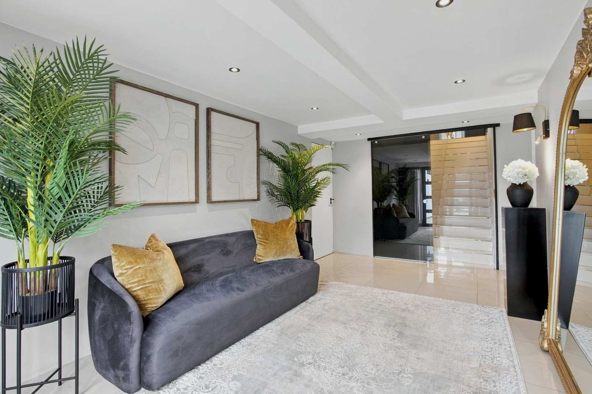 A modern, well-lit living area featuring sleek tiled flooring, recessed ceiling lighting, and a contemporary sliding glass door leading to the staircase.