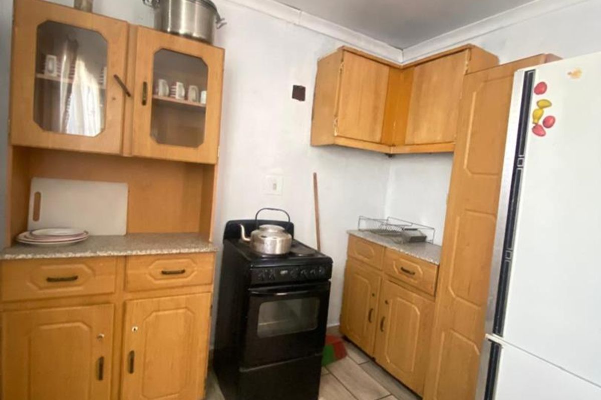 A functional kitchen featuring wooden cabinetry, laminate countertops, a freestanding stove, and tiled flooring, offering potential for modernization and aesthetic updates.