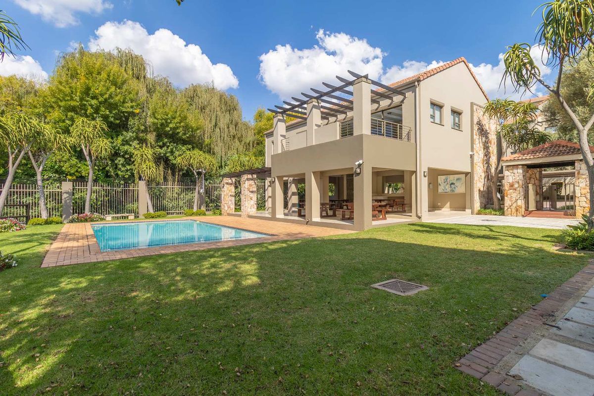 Rear view of the property featuring a well-maintained garden, swimming pool, and a spacious covered patio with a pergola and balcony above.