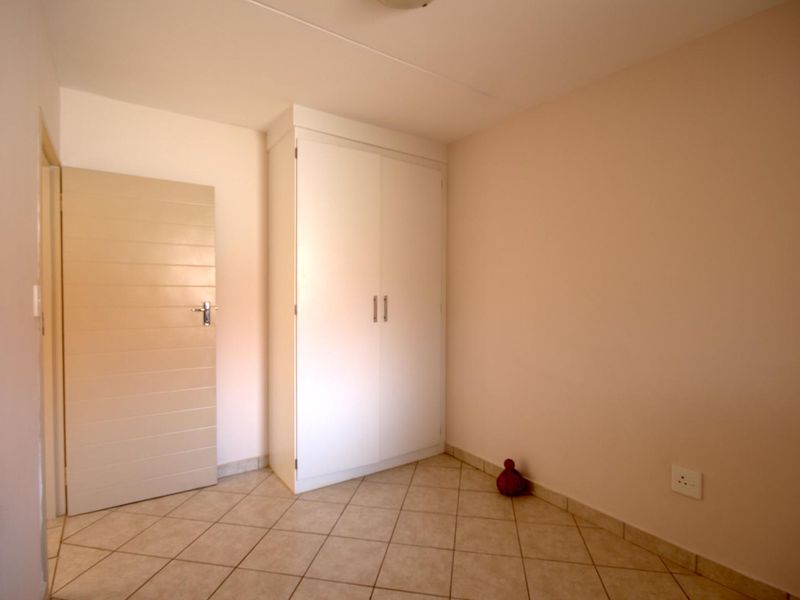 A clean, empty bedroom featuring neutral tiled flooring and a built-in white wardrobe, offering a blank canvas for personalization.