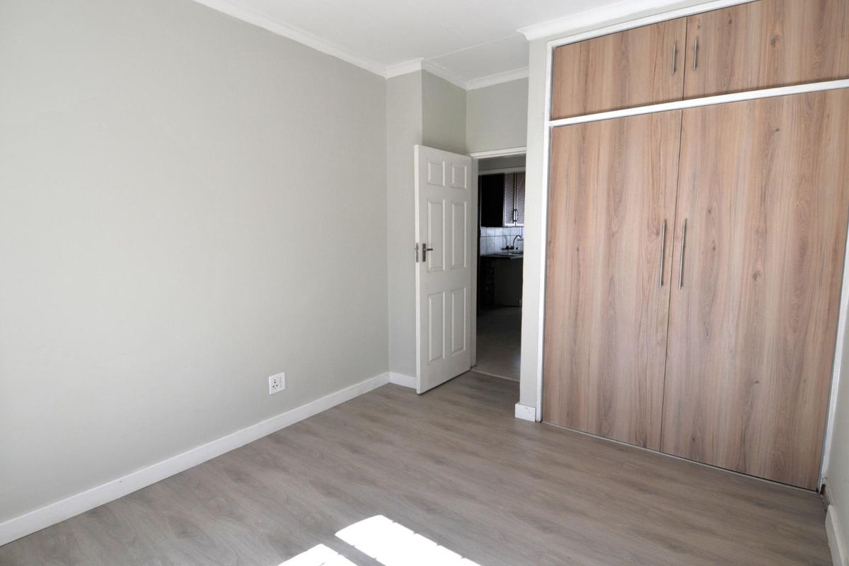A bright, empty bedroom featuring modern wood-look laminate flooring and built-in wooden cabinetry with ample storage space.